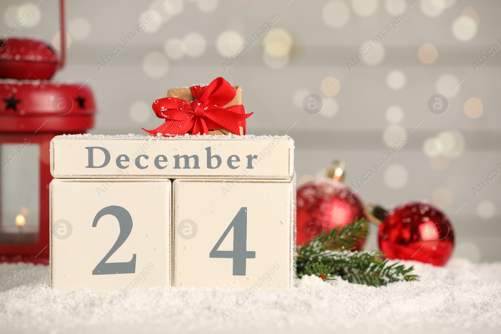 Photo of December 24 - Christmas Eve. Wooden block calendar and festive decor on snow against blurred lights