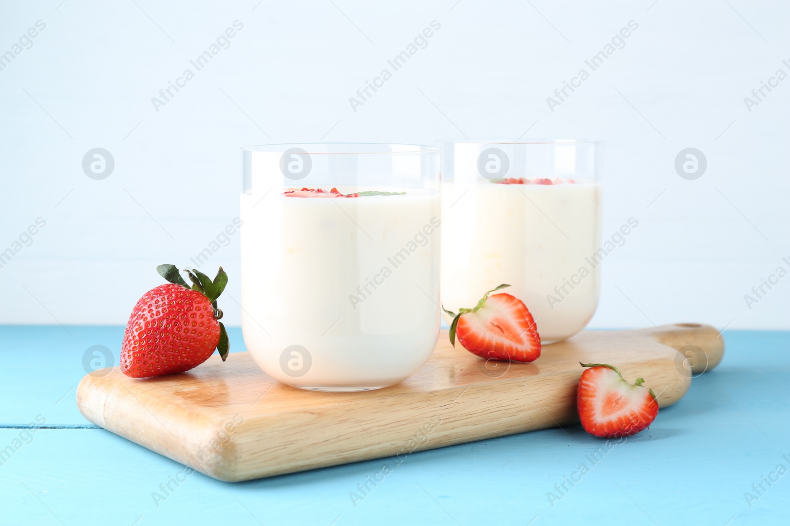 Photo of Tasty yogurt in glasses and strawberries on light blue wooden table