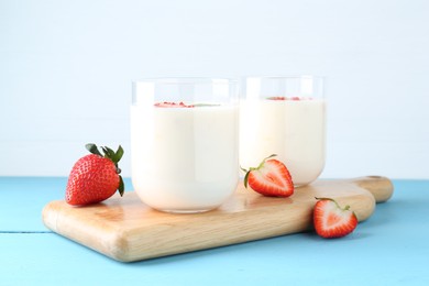 Tasty yogurt in glasses and strawberries on light blue wooden table