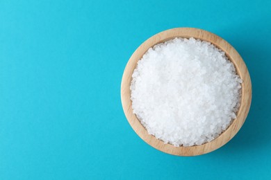 Photo of Organic white salt in bowl on light blue background, top view. Space for text