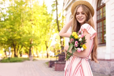 Beautiful teenage girl with bouquet of tulips on city street, space for text