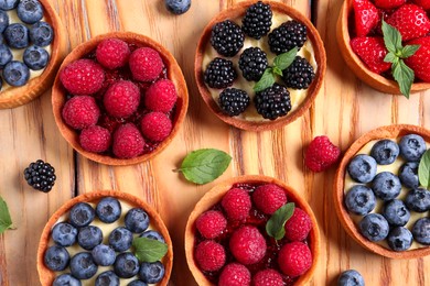 Photo of Tartlets with different fresh berries on wooden table, flat lay. Delicious dessert