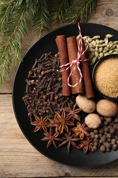 Dishware with different spices and fir branches on wooden table, flat lay