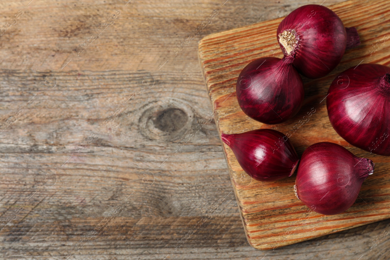 Photo of Board and ripe red onions on wooden table, top view with space for text