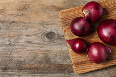 Photo of Board and ripe red onions on wooden table, top view with space for text