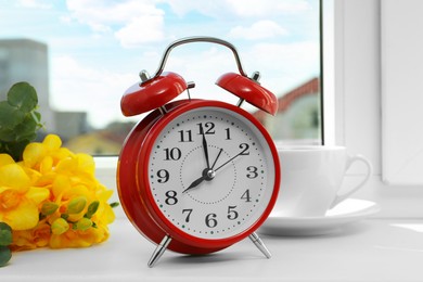 Photo of Alarm clock, beautiful yellow freesias and cup of drink on windowsill. Good morning