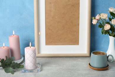 Scented candles, photo frame, flowers and cup on grey table near light blue wall
