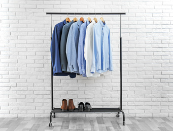 Rack with stylish men's clothes near white brick wall. Space for text