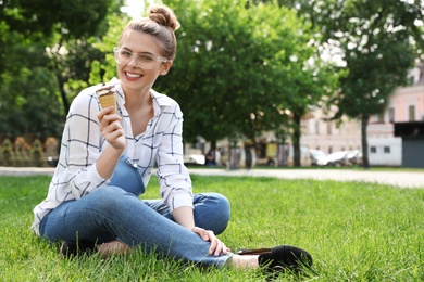Young happy woman with ice cream sitting on grass in park. Space for text