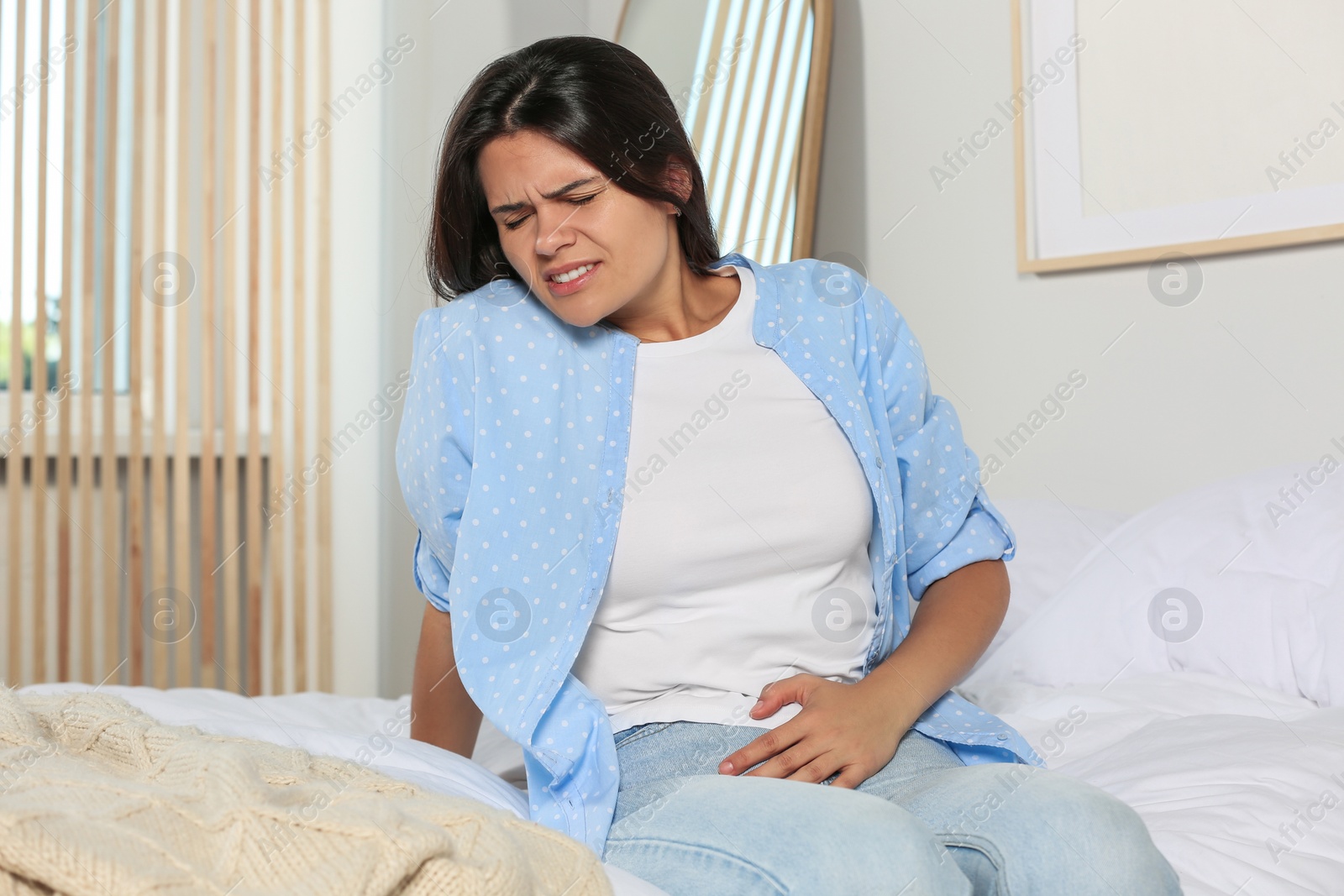 Photo of Young woman suffering from cystitis on bed at home