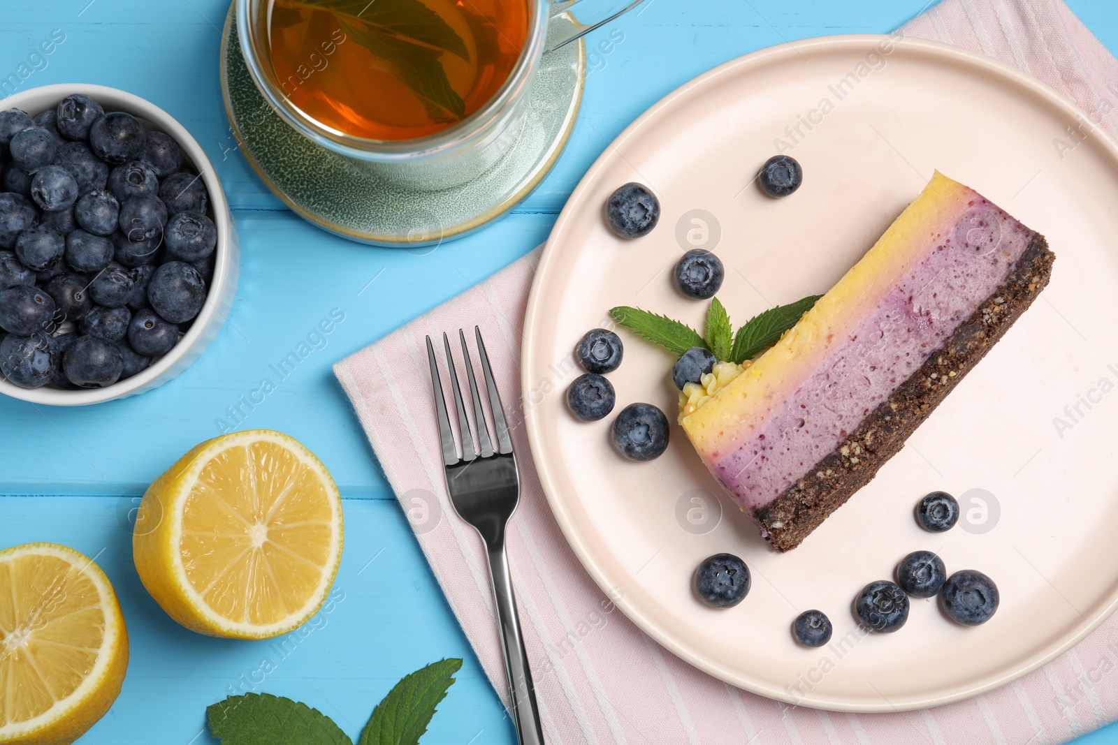 Photo of Delicious cheesecake with blueberry, lemon and tea on light blue wooden table, flat lay