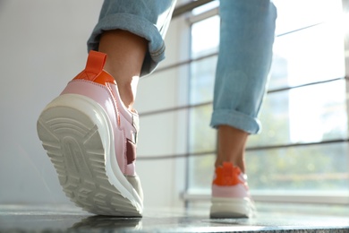 Photo of Young woman wearing stylish sneakers on staircase indoors, closeup