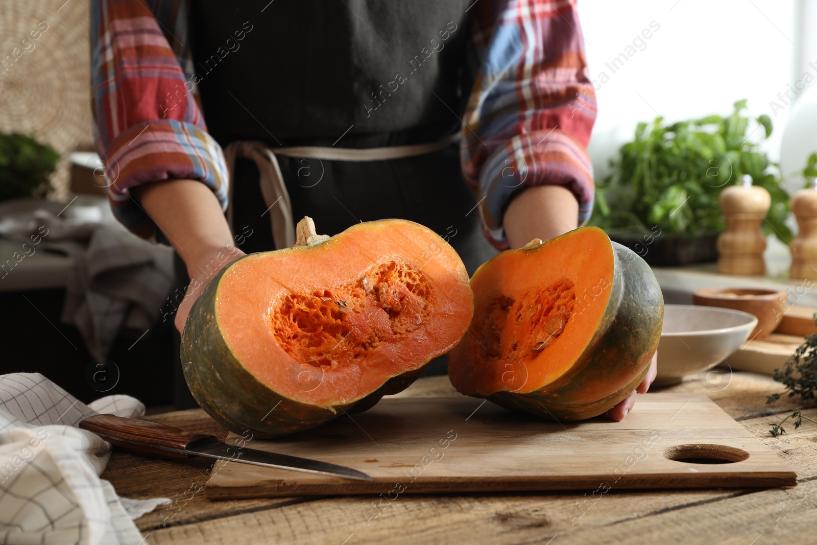 Photo of Woman with cut fresh ripe pumpkin at wooden table in kitchen, closeup