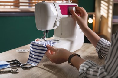 Photo of Woman sewing cloth protective mask with machine at table indoors, closeup