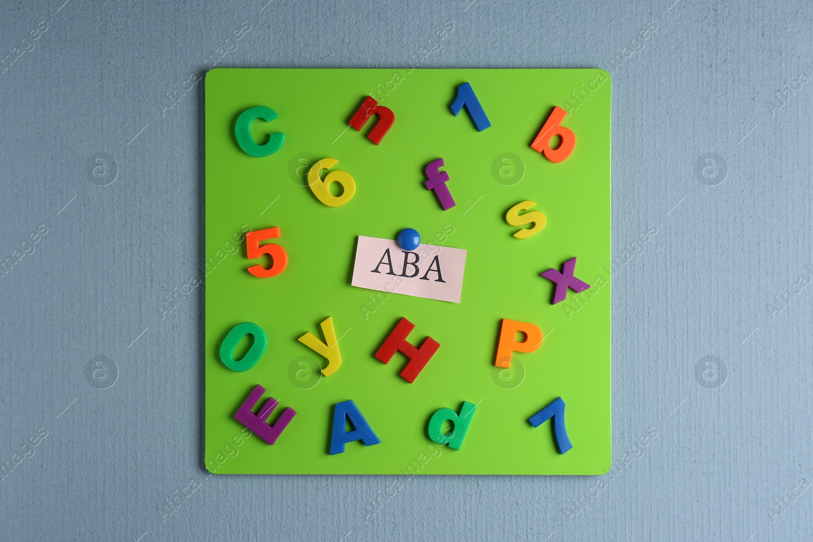Photo of Magnetic board with abbreviation ABA (Applied behavior analysis), colorful letters and numbers on light grey wall