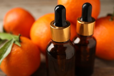 Photo of Bottles of tangerine essential oil and fresh fruits on table, closeup