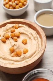 Photo of Bowl with delicious hummus and chickpeas on light wooden table, closeup