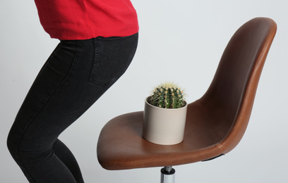 Woman sitting down onto chair with cactus against white background, closeup. Hemorrhoids concept