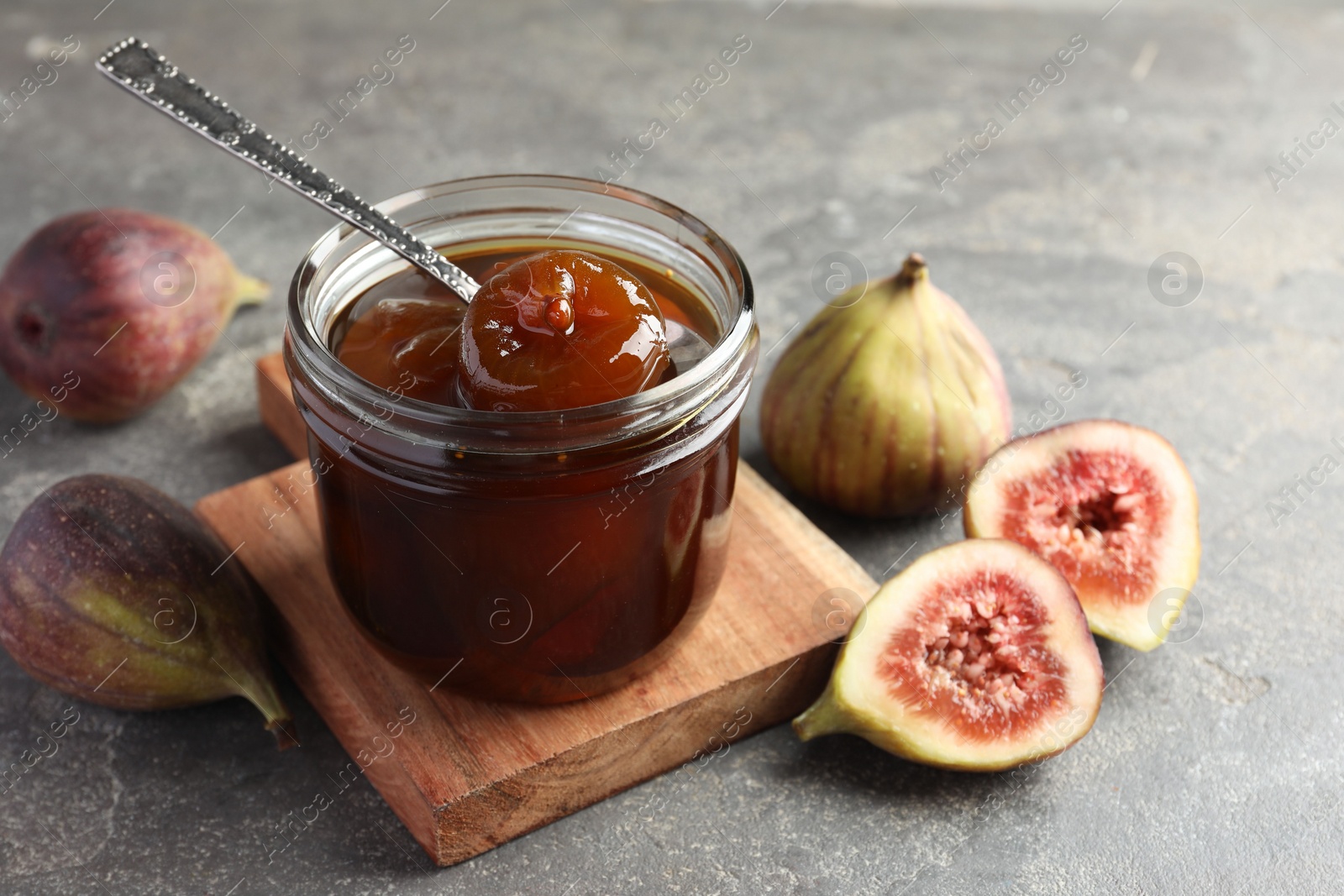 Photo of Jar of tasty sweet jam and fresh figs on grey table