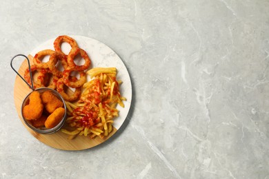 French fries, tasty chicken nuggets and fried onion rings with ketchup on light grey marble table, top view. Space for text