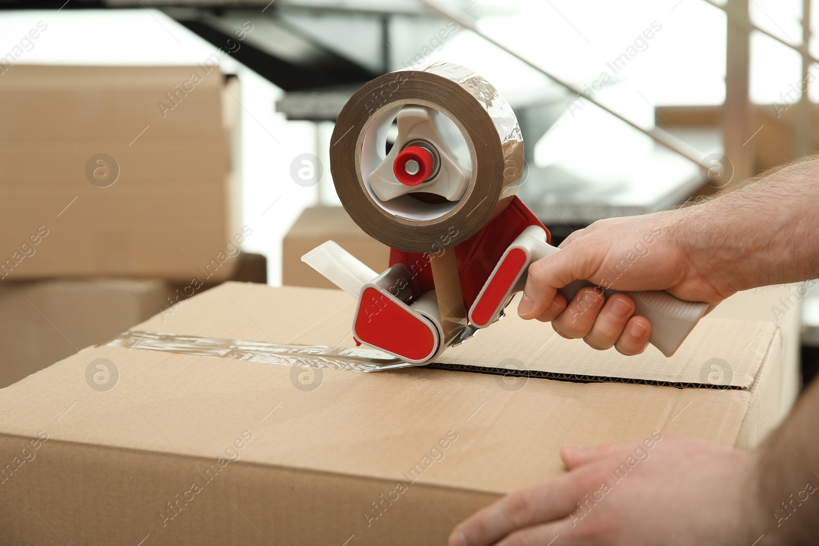 Photo of Worker taping cardboard box indoors, closeup view