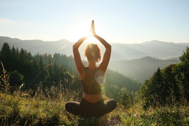 Photo of Woman practicing yoga in mountains at sunrise, back view