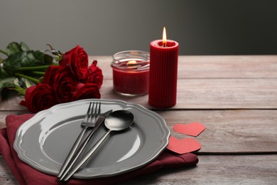 Romantic place setting with red roses, candles and decorative hearts on wooden table, space for text. St. Valentine's day dinner