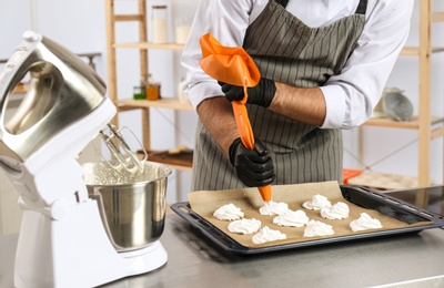 Photo of Pastry chef preparing meringues at table in kitchen, closeup