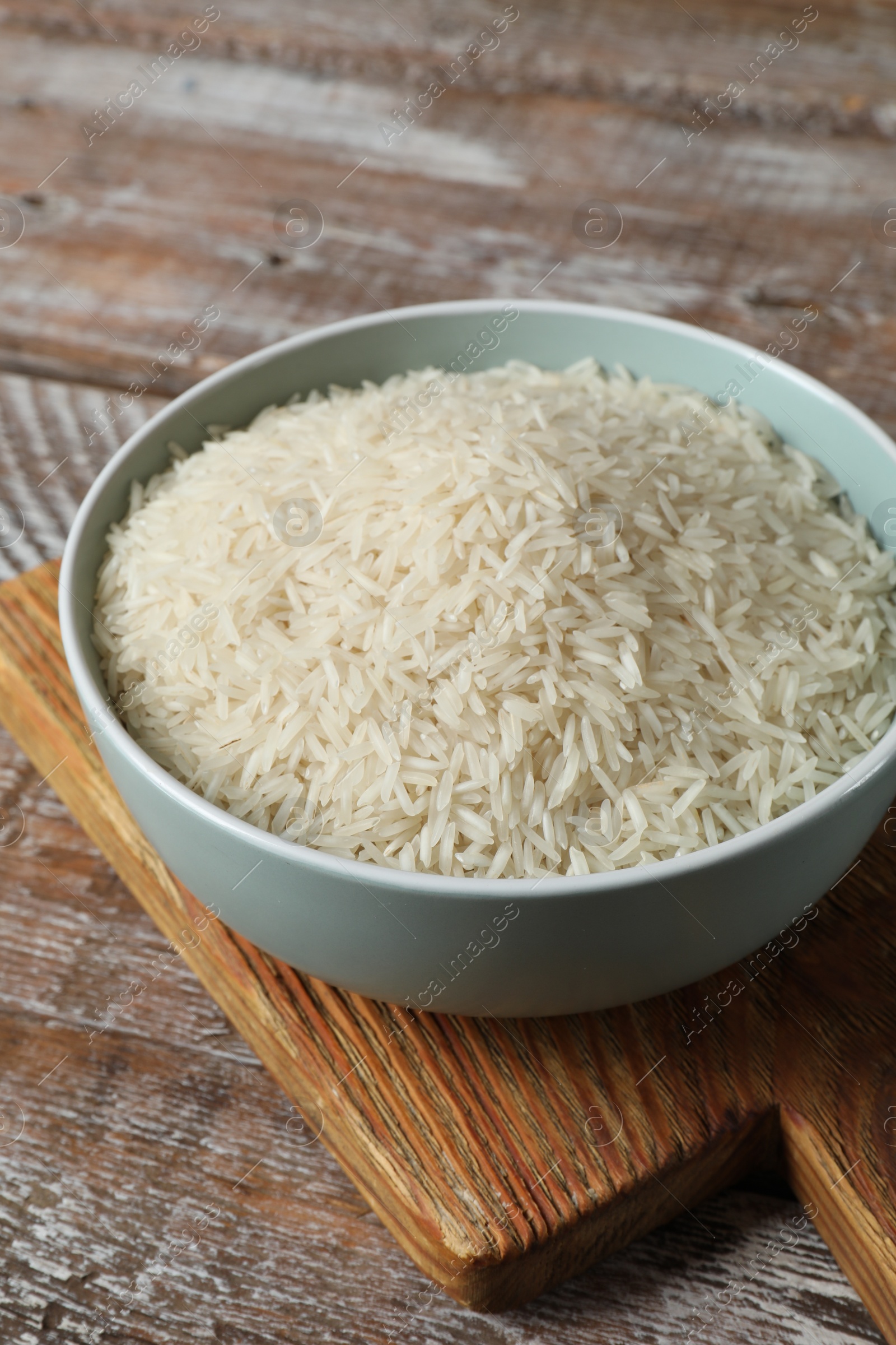 Photo of Raw basmati rice in bowl on wooden table, closeup