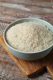 Photo of Raw basmati rice in bowl on wooden table, closeup