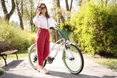 Beautiful woman with bicycle and bouquet of yellow tulips outdoors on sunny spring day