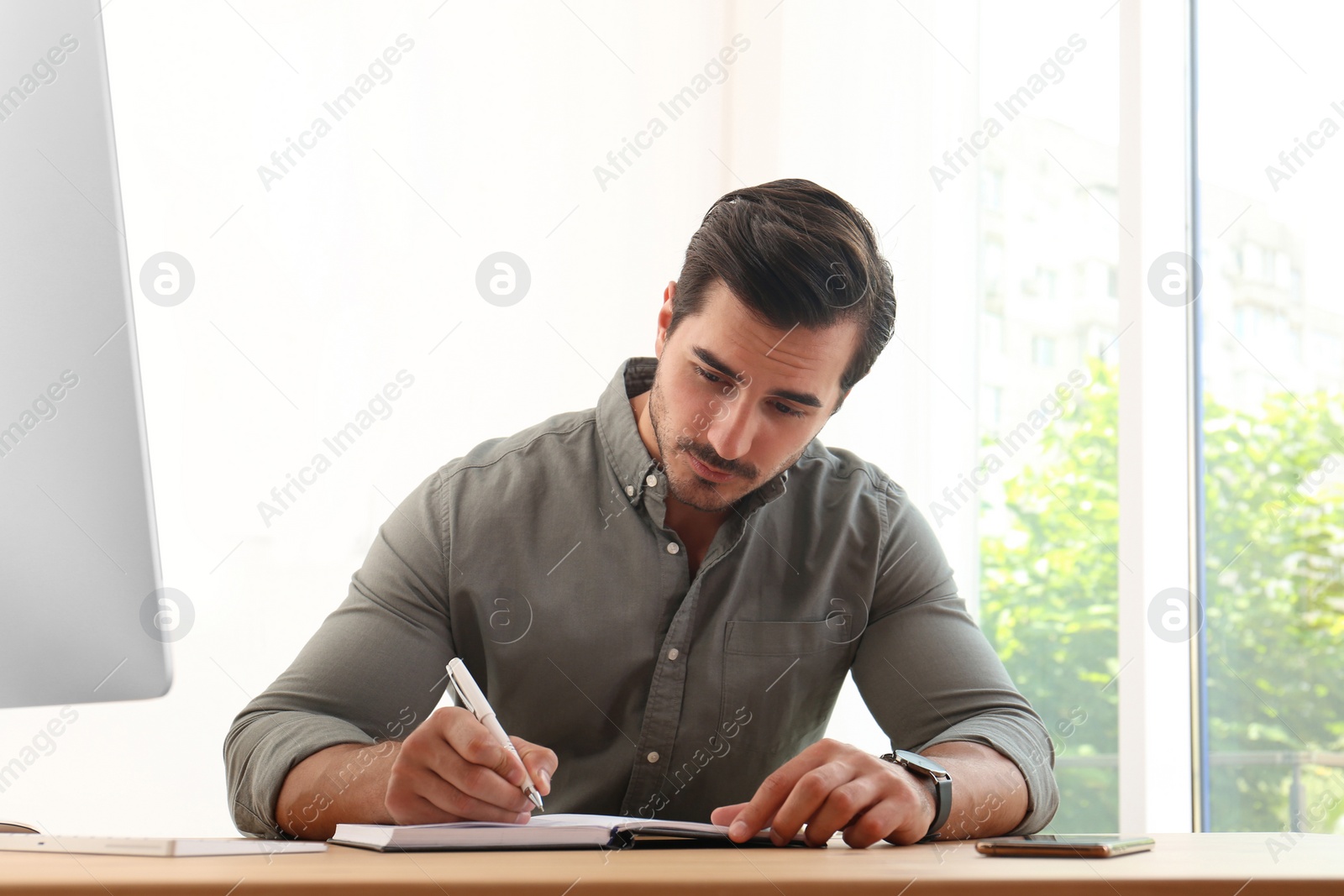 Photo of Handsome young man working with notebook at table in office