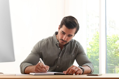 Handsome young man working with notebook at table in office