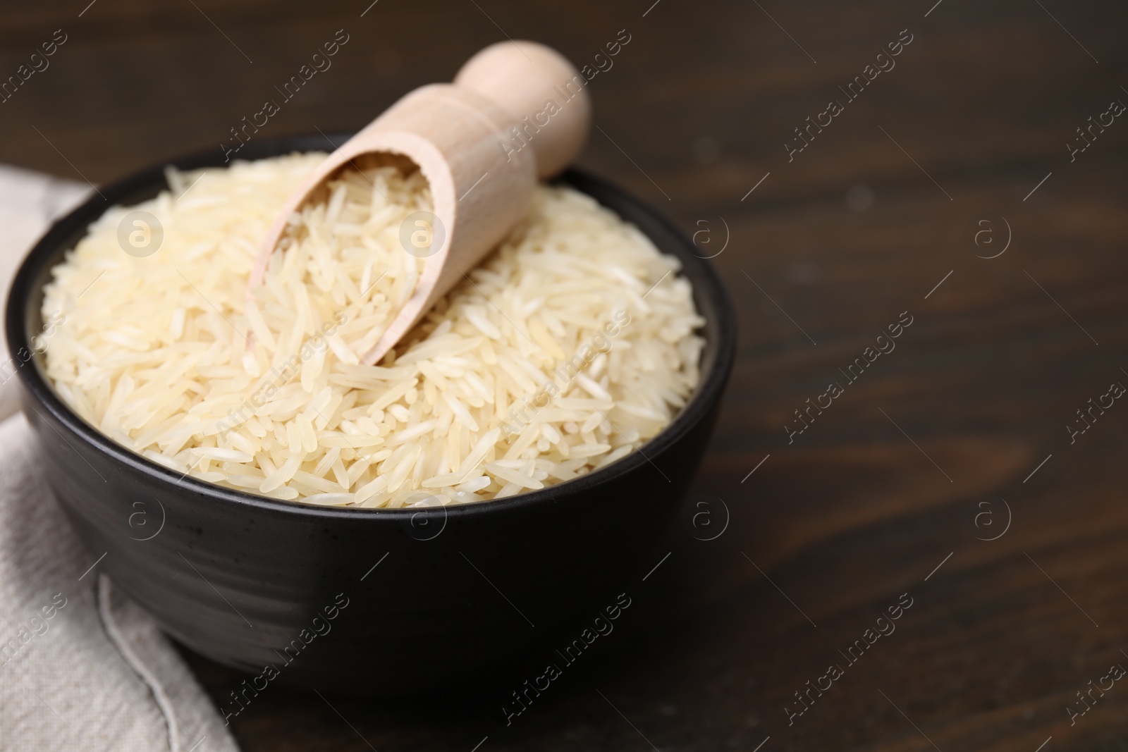 Photo of Bowl and scoop with raw rice on wooden table, closeup. Space for text