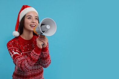 Photo of Young woman in Christmas sweater and Santa hat shouting in megaphone on light blue background. Space for text