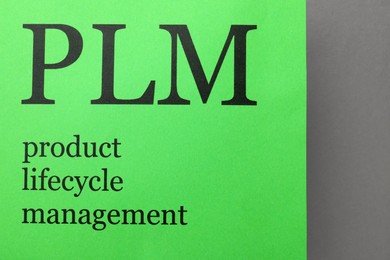 Green paper with abbreviation PLM (Product Lifecycle Management) on grey background, top view