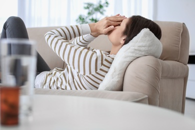 Photo of Young woman suffering from headache on sofa at home