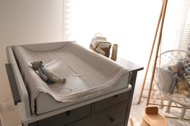 Photo of Chest of drawers with changing pad and tray in nursery. Baby room interior design
