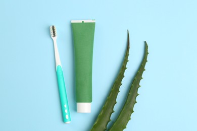 Tube of toothpaste, toothbrush and fresh aloe on light blue background, flat lay