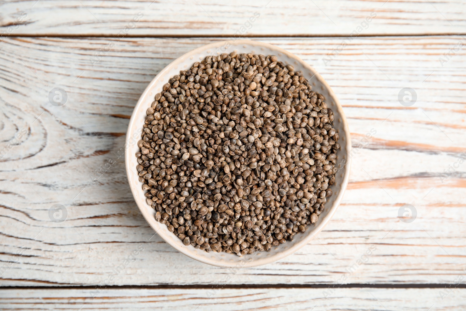 Photo of Bowl with organic hemp seeds on white wooden table, top view