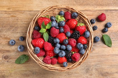 Photo of Many different fresh ripe berries in wicker basket on wooden table, flat lay