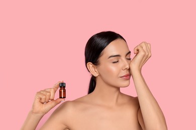 Photo of Young woman smelling essential oil on wrist against pink background