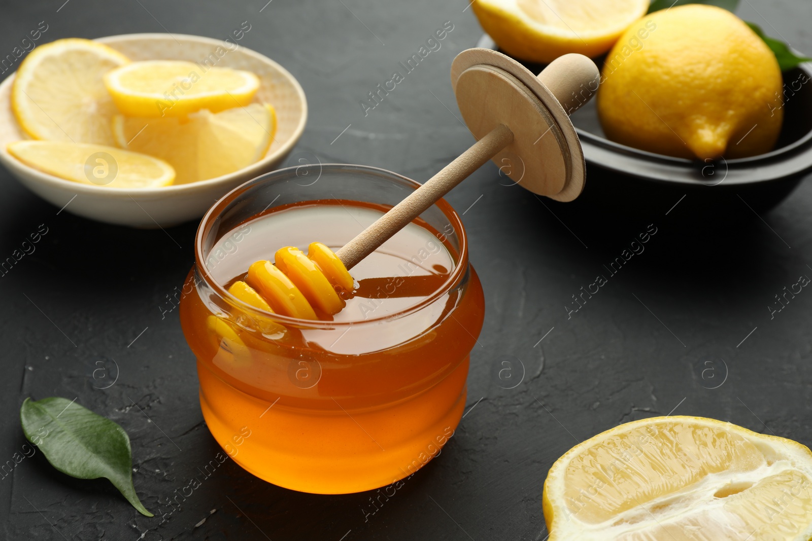 Photo of Sweet honey and fresh lemons on black table, closeup