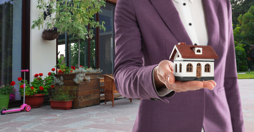 Image of Real estate agent with model against modern house, space for text. Banner design, closeup 