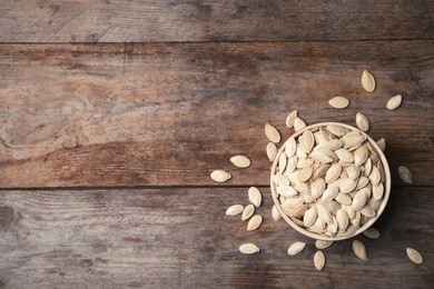 Photo of Raw pumpkin seeds in bowl on wooden background, top view. Space for text