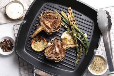 Photo of Tasty grilled artichokes served on white table, flat lay