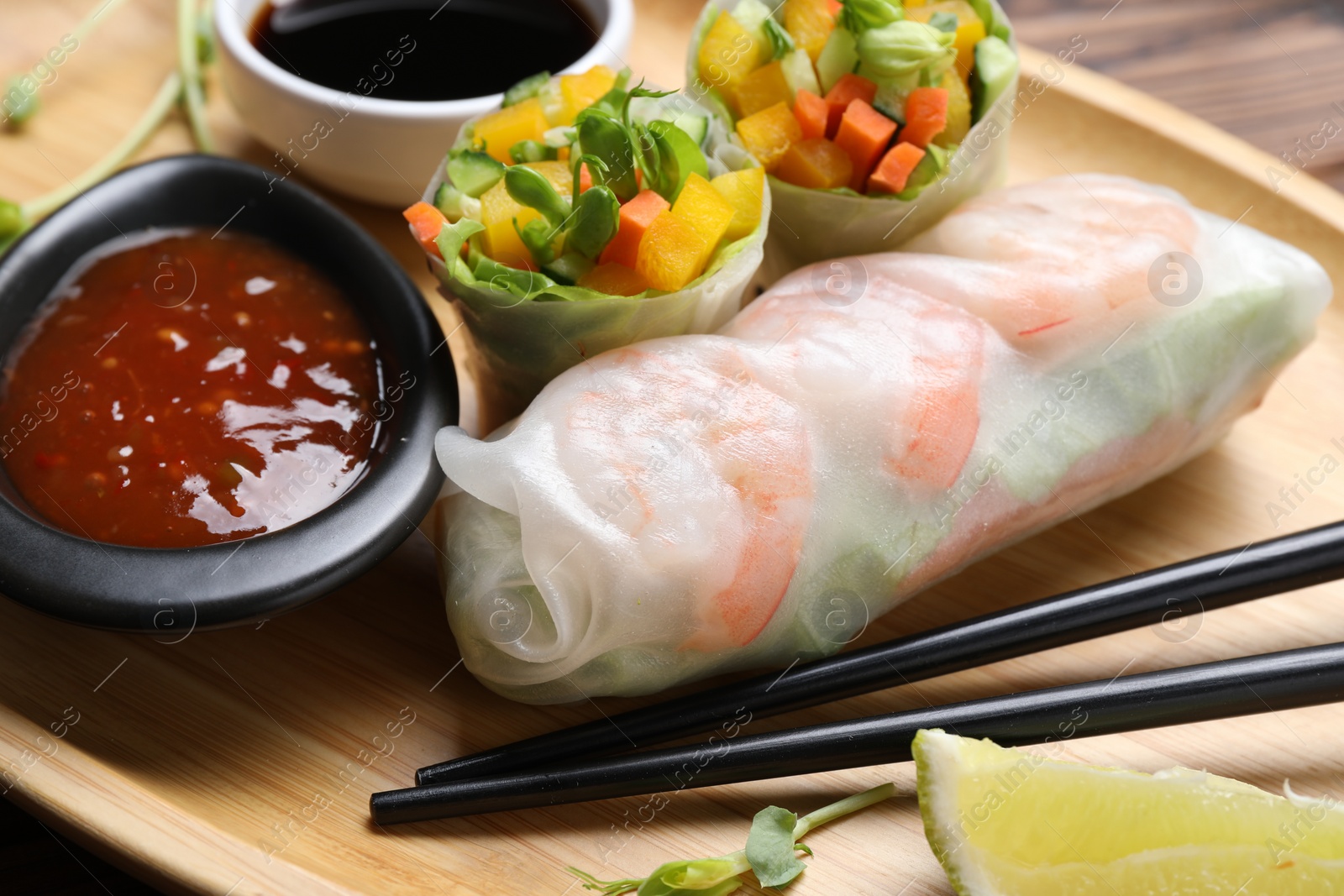 Photo of Tasty spring rolls and sauces on wooden plate, closeup