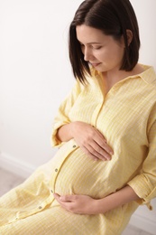 Beautiful pregnant woman sitting in light room