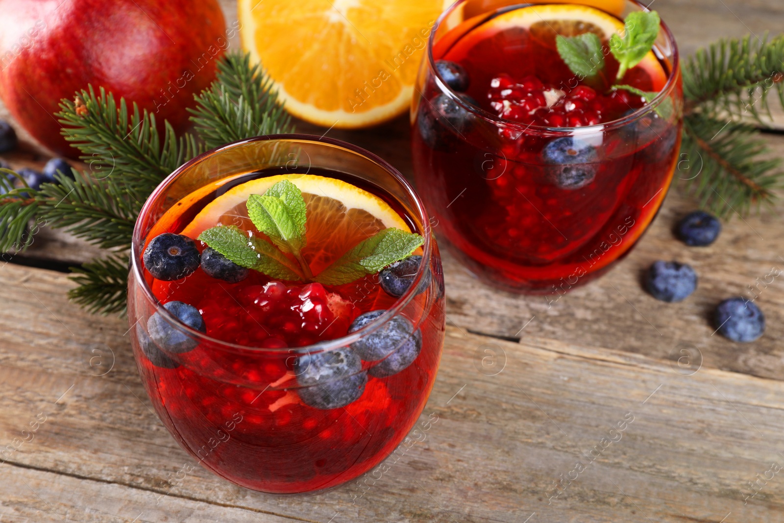 Photo of Aromatic Christmas Sangria drink in glasses, fir branches and ingredients on wooden table