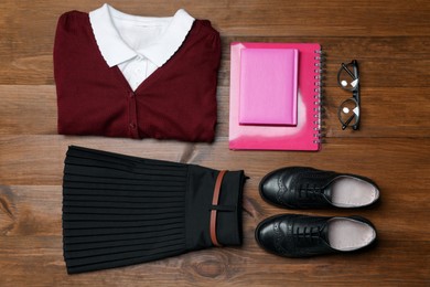 Stylish school uniform, glasses and notebooks on wooden background, flat lay